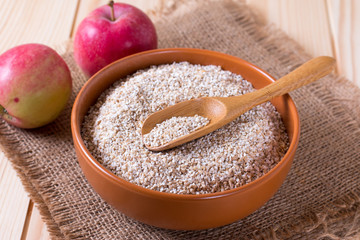 Spelt in a wooden bowl and spoon on a wooden background