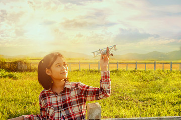 Naklejka na ściany i meble Pretty Asian girl and toy airplane in hand at the farm field sunset.