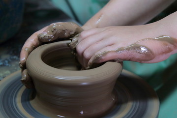 Hands of a potter, creating an earthen jar on pottery wheel.