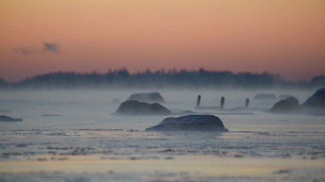 Almost frozen water waving slowly in the icy Baltic Sea at sunset time in Helsinki, Finland with sea fog arising from the water on 6 January 2016