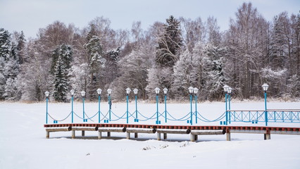 Winter landscape with forest and snow-covered pier on lake