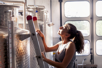 female winemaker controls the quality of wine on ladder over tan