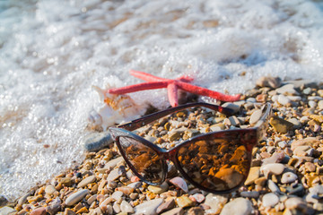 starfish and sunglasses on the shore of the sea in the background