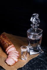 Bottle and shot glasses with vodka with slices of smoked meat on