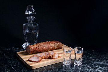 Bottle and shot glasses with vodka with slices of smoked meat on