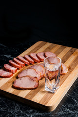 Shot glasses with vodka, slices of smoked meat and smoked sausag