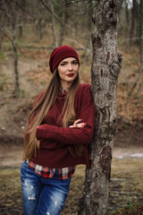 young beautiful woman in burgundy hat and sweater posing in the forest among the trees