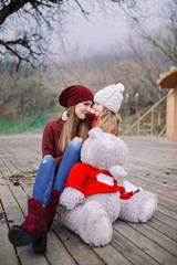 beautiful young woman hugging little girl with big teddy bear. mother and daughter enjoy life outdoor