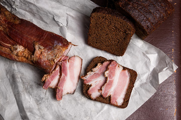 Puff smoked bacon with rye black bread on the packaging paper. V