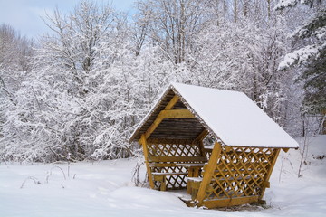 Little wooden gazebo in the winter snowy forest