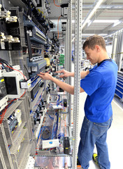 Montage von Elektronik in einer Fabrik - junger Mann arbeitet an einem Schaltschrank // Montage of...