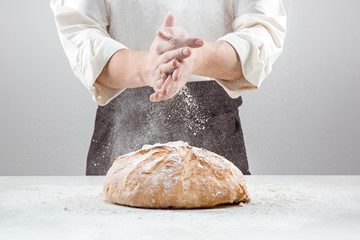 Les mains masculines dans la farine et la miche de pain biologique rustique