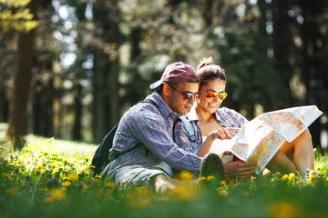 Couple hiking. Young couple sitting on grass and examining the map.