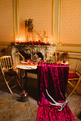 Table setting at wedding reception in the evening. Floral compositions and candles on decorated dining table by the fireplace. Love, romance concept.