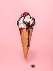 melting ice cream cone with chocolate syrup and cranberry isolated on pink background