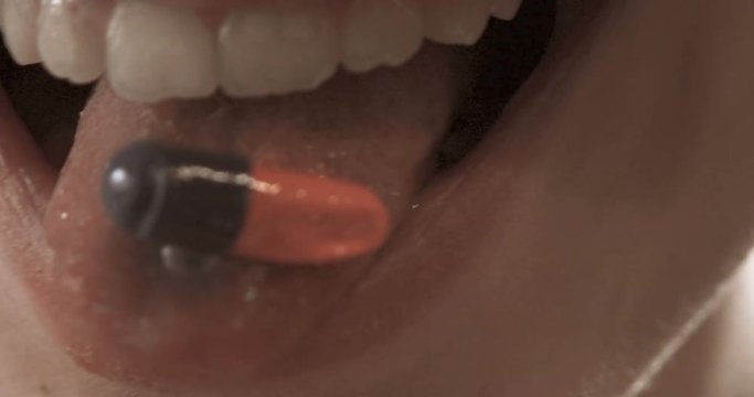 Orange-blue pill on tongue of young woman closeup