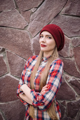 portrait of beautiful young woman in burgundy hat and plaid shirt against the backdrop of a stone wall