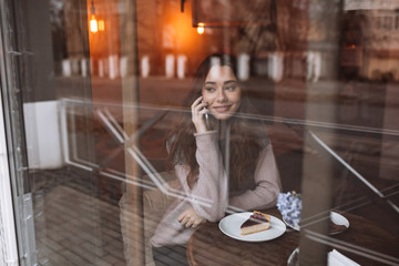 Happy young woman in cafe while talking by her phone