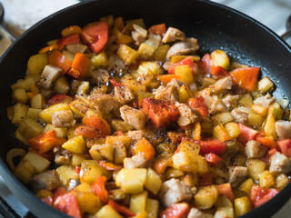 Picture of the frying colourful meal in the frying pan close up. Black frying pan on a white gas stove.