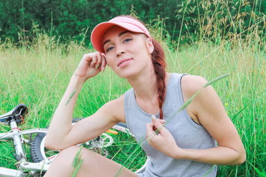 Girl with a beautiful smile sitting on the grass next to his bik