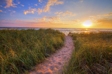 Obraz premium Ścieżka Do Letniej Plaży Zachodu Słońca. Kręta ścieżka przez trawę wydmową prowadzi do plaży o zachodzie słońca na wybrzeżu śródlądowego morza jeziora Michigan. Park Stanowy Hoffmaster. Muskegon w stanie Michigan.