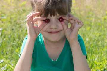Happy little cute gitl holds two cherries at summer day outdoor,