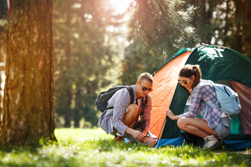 The couple sets up their camping tent, ready to embrace the outdoors together. - obrazy, fototapety, plakaty