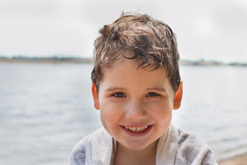 Happy handsome little boy smiles near river shore at sunny day