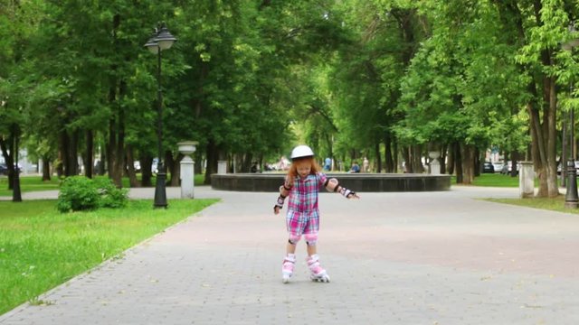 Cute little girl in helmet roller skates in green summer park