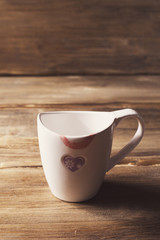 White Cup with painted heart and lipstick, Valentine's day, on the background of old wooden planks
