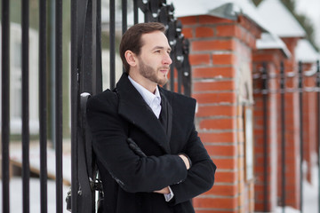 Fototapeta premium Male businessman sitting on a bench, holding a business briefcase with documents, in the winter on the street