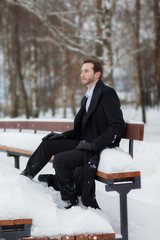 Male businessman sitting on a bench, holding a business briefcase with documents, in the winter on the street