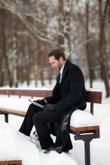 Male businessman sitting on a bench, holding a business briefcase with documents, in the winter on the street