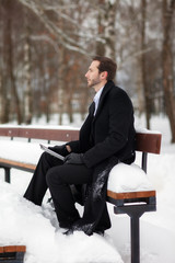 Male businessman sitting on a bench, holding a business briefcase with documents, in the winter on the street