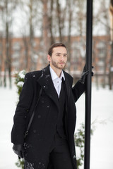 Male businessman sitting on a bench, holding a business briefcase with documents, in the winter on the street