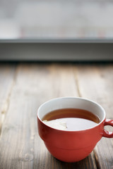 On old vintage boards is a red Cup with tea and lemon, next to the fabric heart behind the rose petals toned