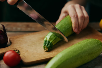 Macro shot of chef cutting fresh raw zucchini on board in the kitchen. 