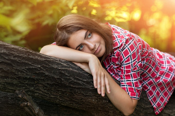 Young beautiful girl in plaid shirt sitting on a tree in the Park on a Sunny summer day in the bushes, reading a book, fantasizing, thinking, dreaming, looking up