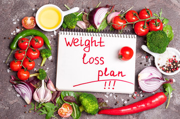 Fresh organic vegetables, herbs and spices. Mix salad, tomatoes, chilli, garlic and notebook with plan eating. Weight loss concept. Products for boosting metabolism. Top view