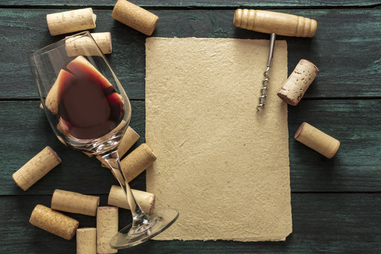 Red wine glass, corks, corkscrew and parchment with copyspace