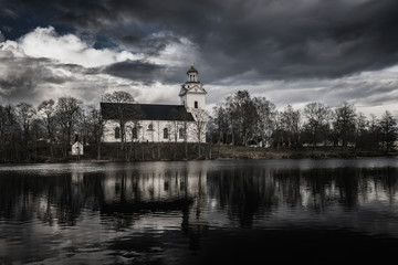 Fototapeta na wymiar White church in a dark and scary environment with black water and a dramatic cloudy sky
