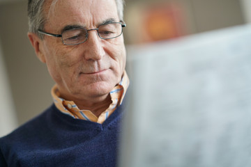 Smiling senior man with eyeglasses reading newspaper