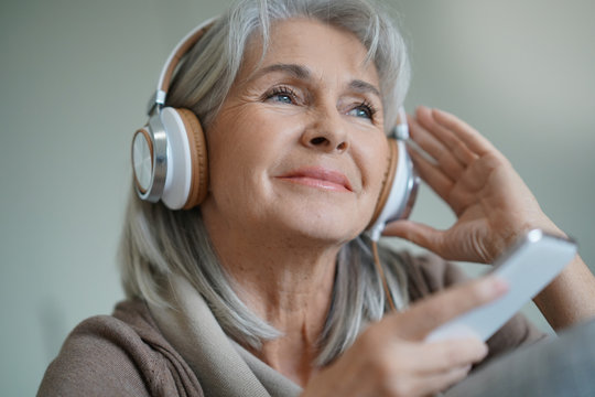 Senior woman at home listening to music with smartphone