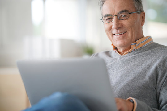 Senior man with eyeglasses connected on laptop at home
