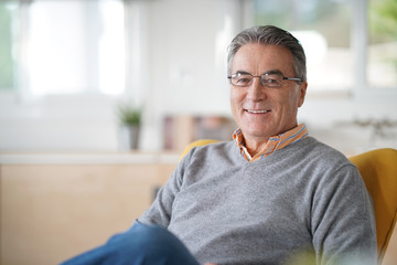 Smiling senior man with eyeglasses relaxing in armchair - Powered by Adobe