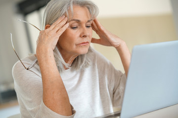 Senior woman in front of laptop, having a headache