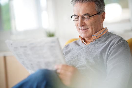 Smiling senior man with eyeglasses reading newspaper