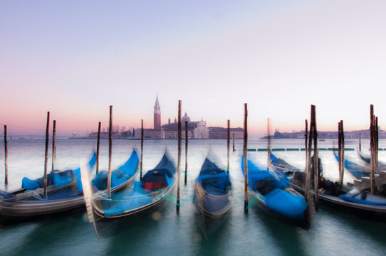 Traditional Venetian gondolas moored on the waterfront of Venice, Italy. Captured during sunset with motion blur.