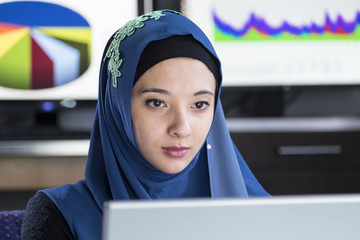 Young woman wearing a hijab working at a computer, close up shot © Burlingham