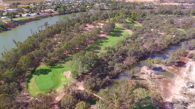 Aerial view of Golfers in electric Golf Buggy with Caddy driving through bush land Golf Course by river.